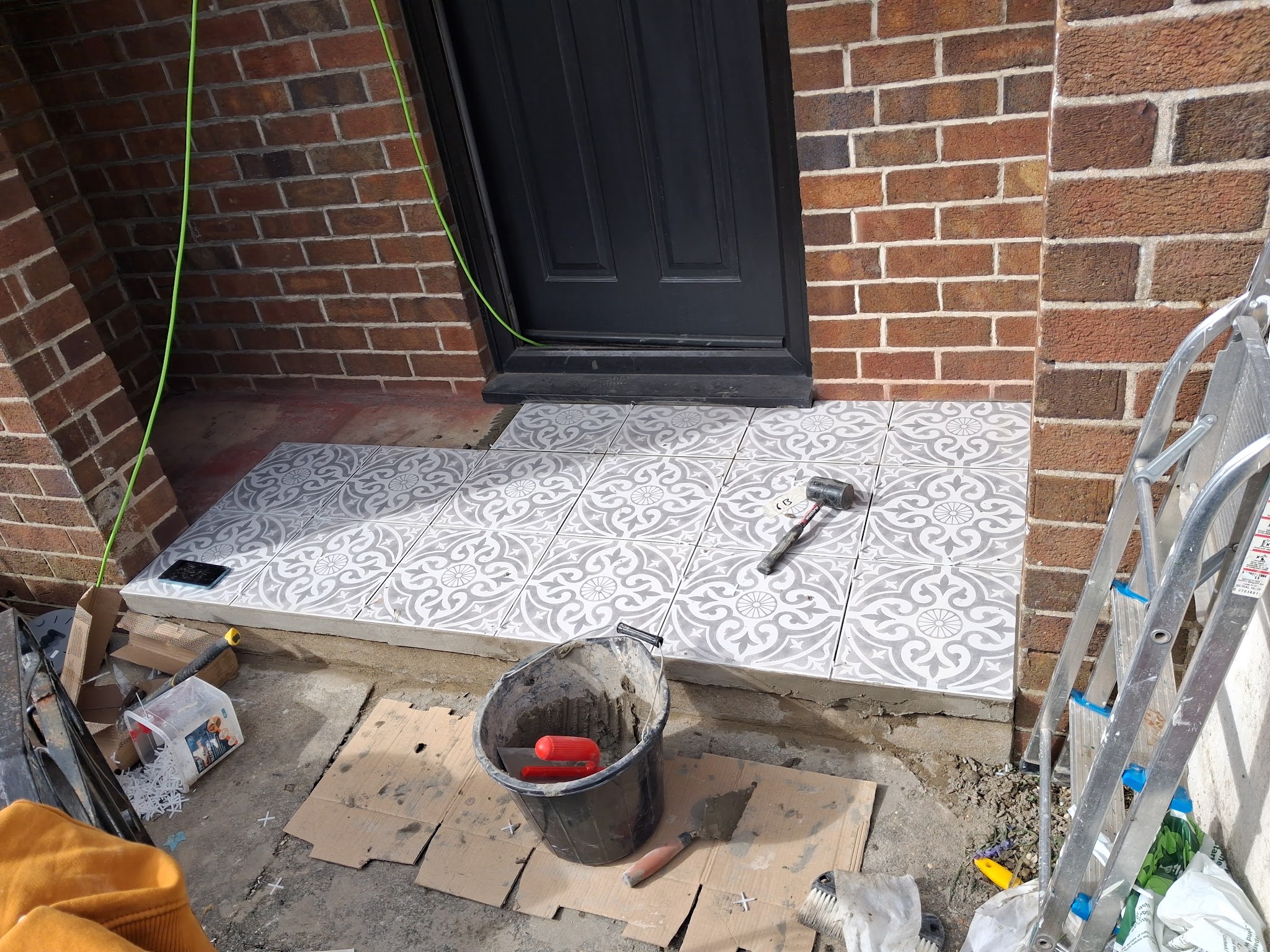 Patterned grey and white tiles being laid on a front step