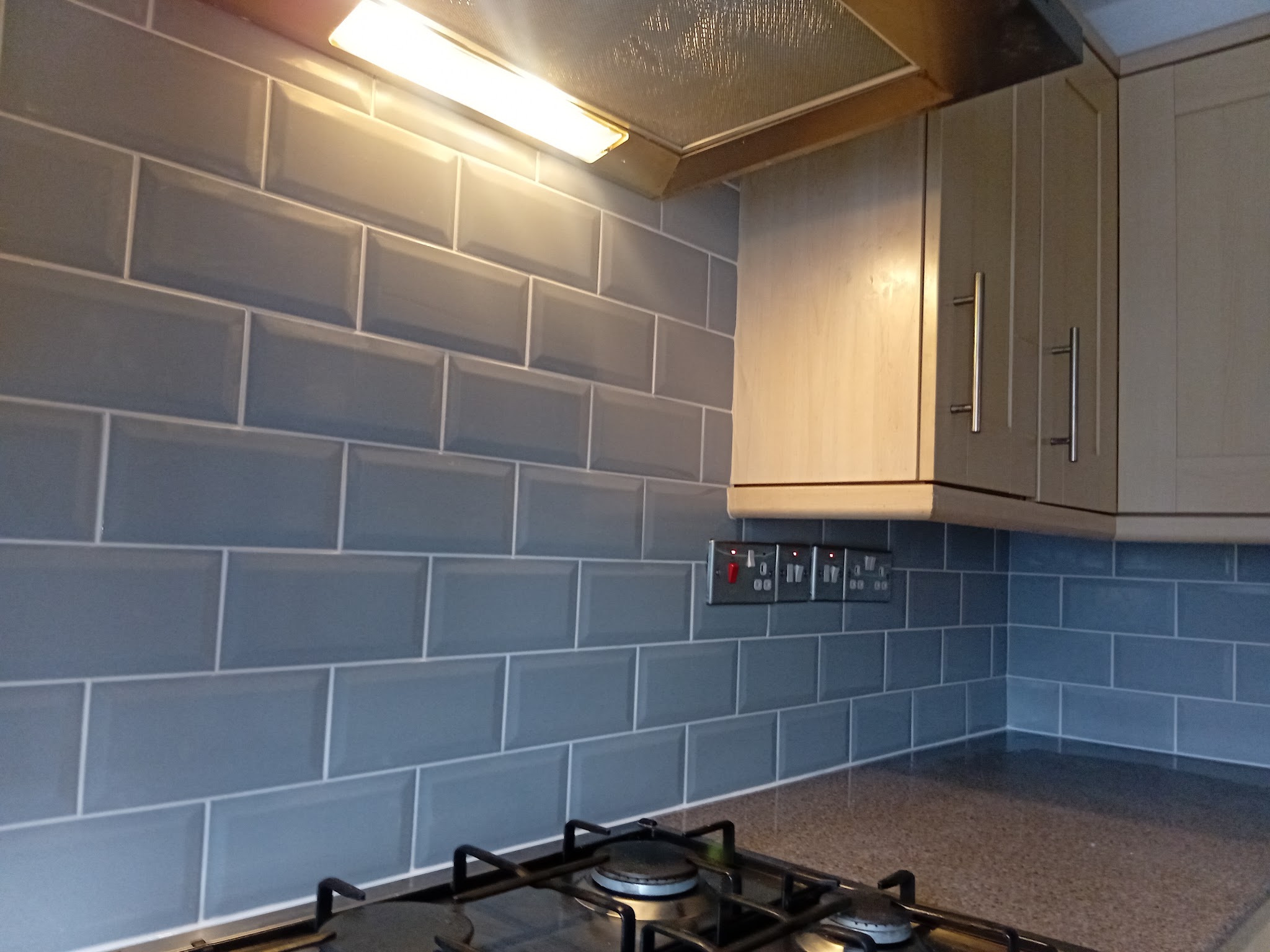 Blue metro-tile splashback behind a gas hob